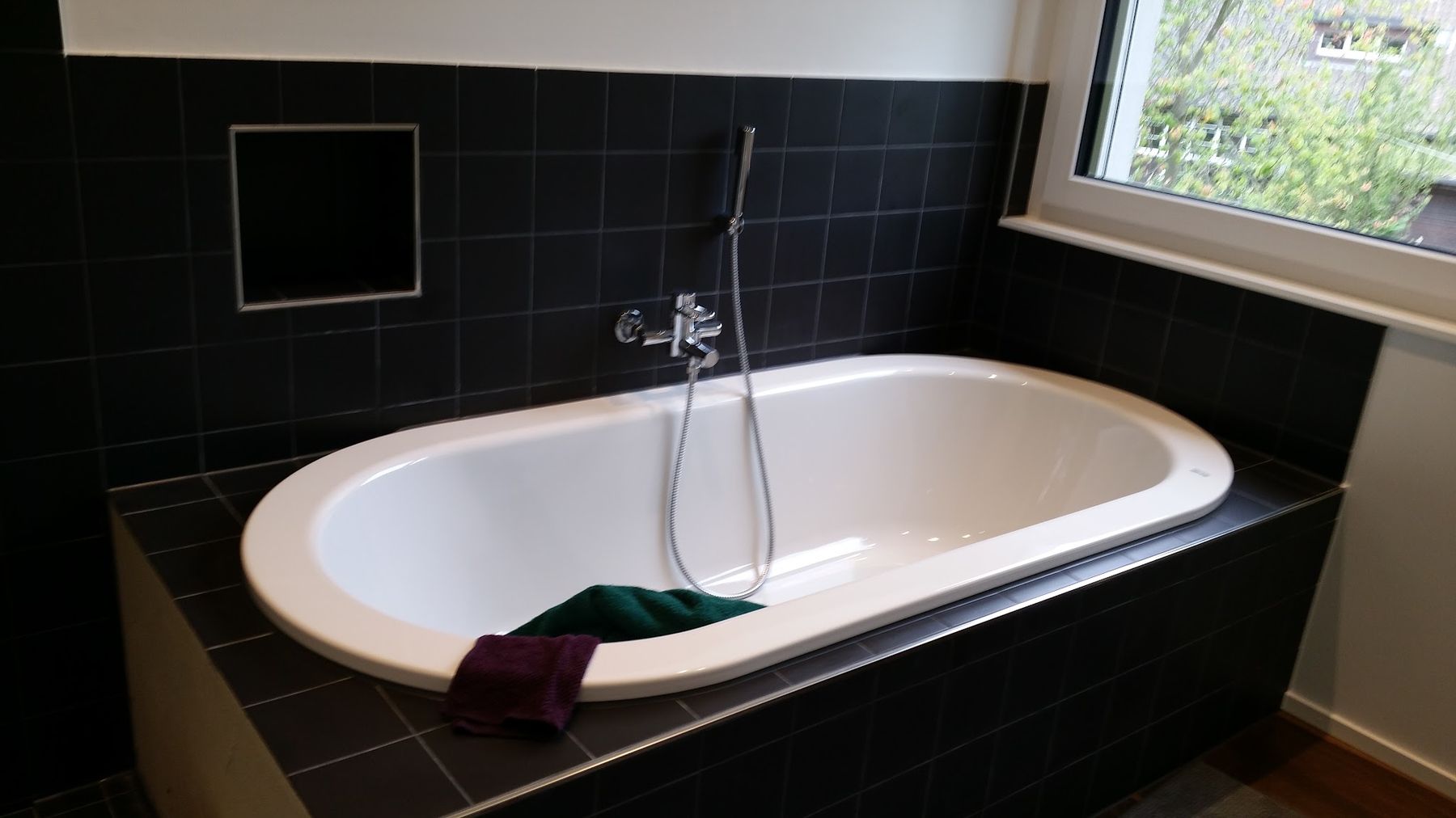 Badewanne mit schwarz verfliester Wannenverkleidung vor dem Fenster