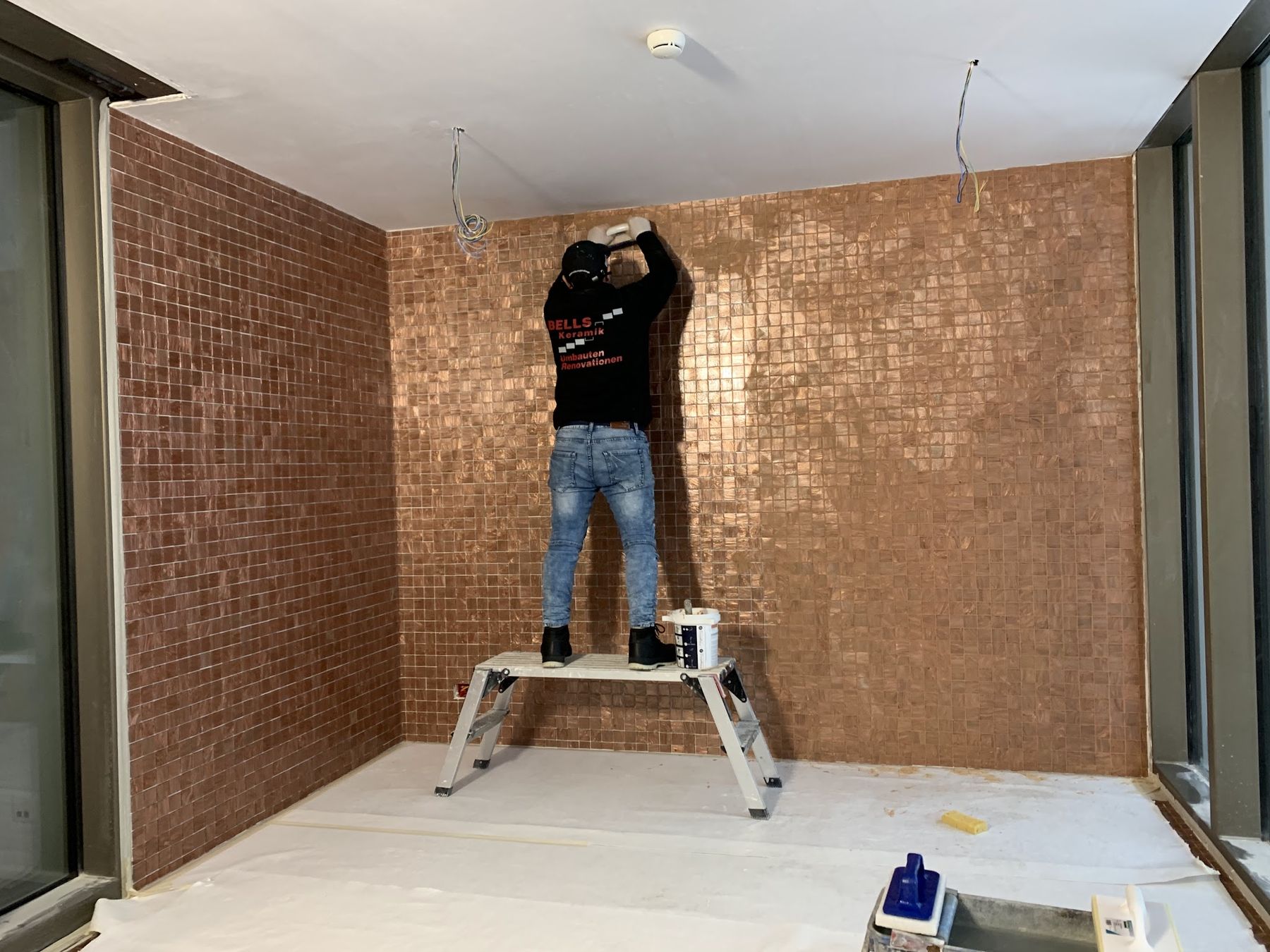 Plattenleger verlegt ein kupferfarbenes Mosaik an einer Wand