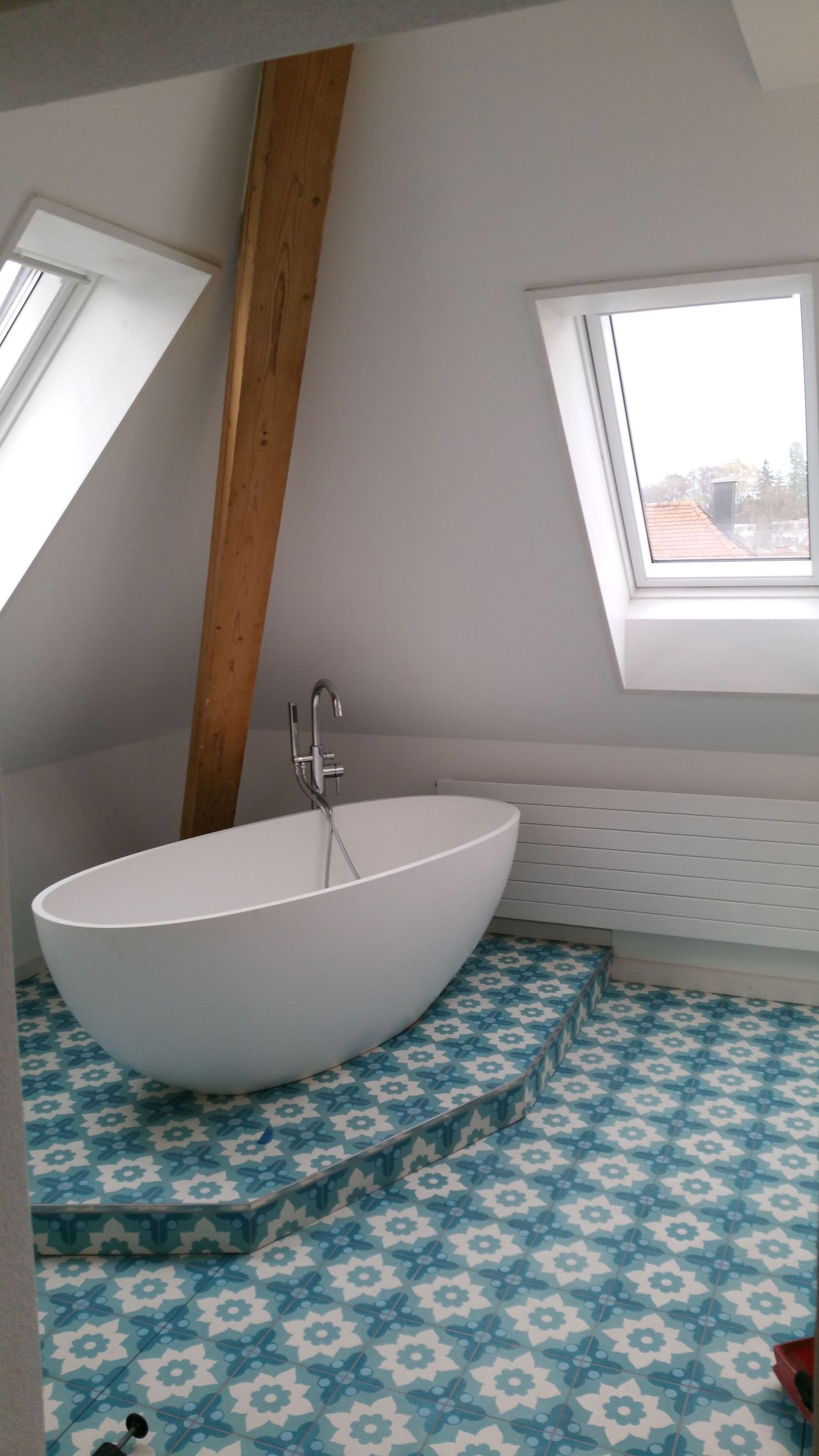 Freistehende Wanne auf blauem Fliesenpodest unter einem Dachfenster